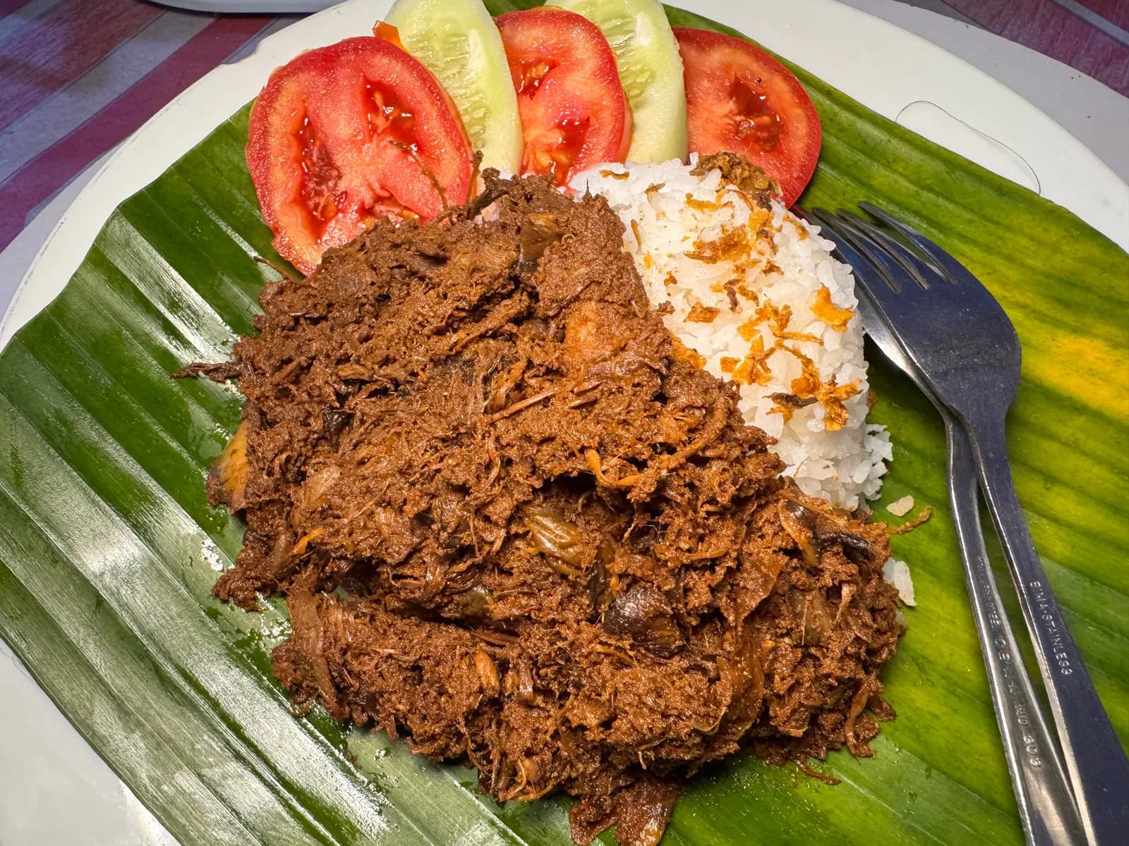 Rendang jantung pisang dengan nasi, tomat, dan timun di atas daun pisang