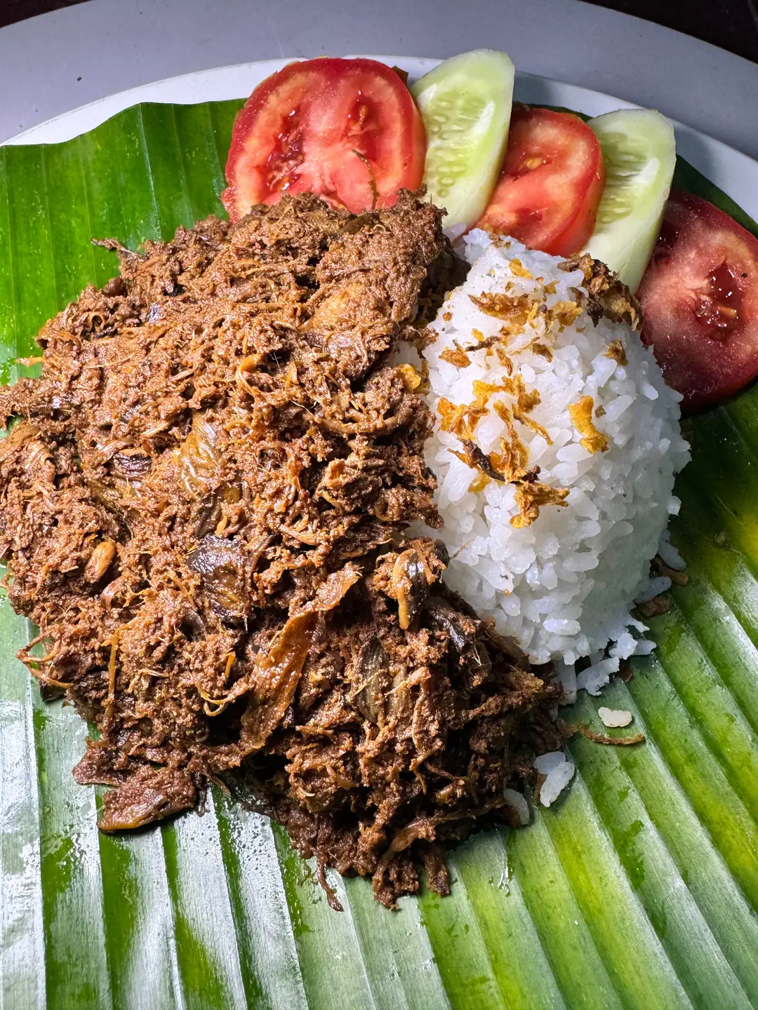 Rendang jantung pisang dengan nasi putih, tomat, dan timun di atas daun pisang